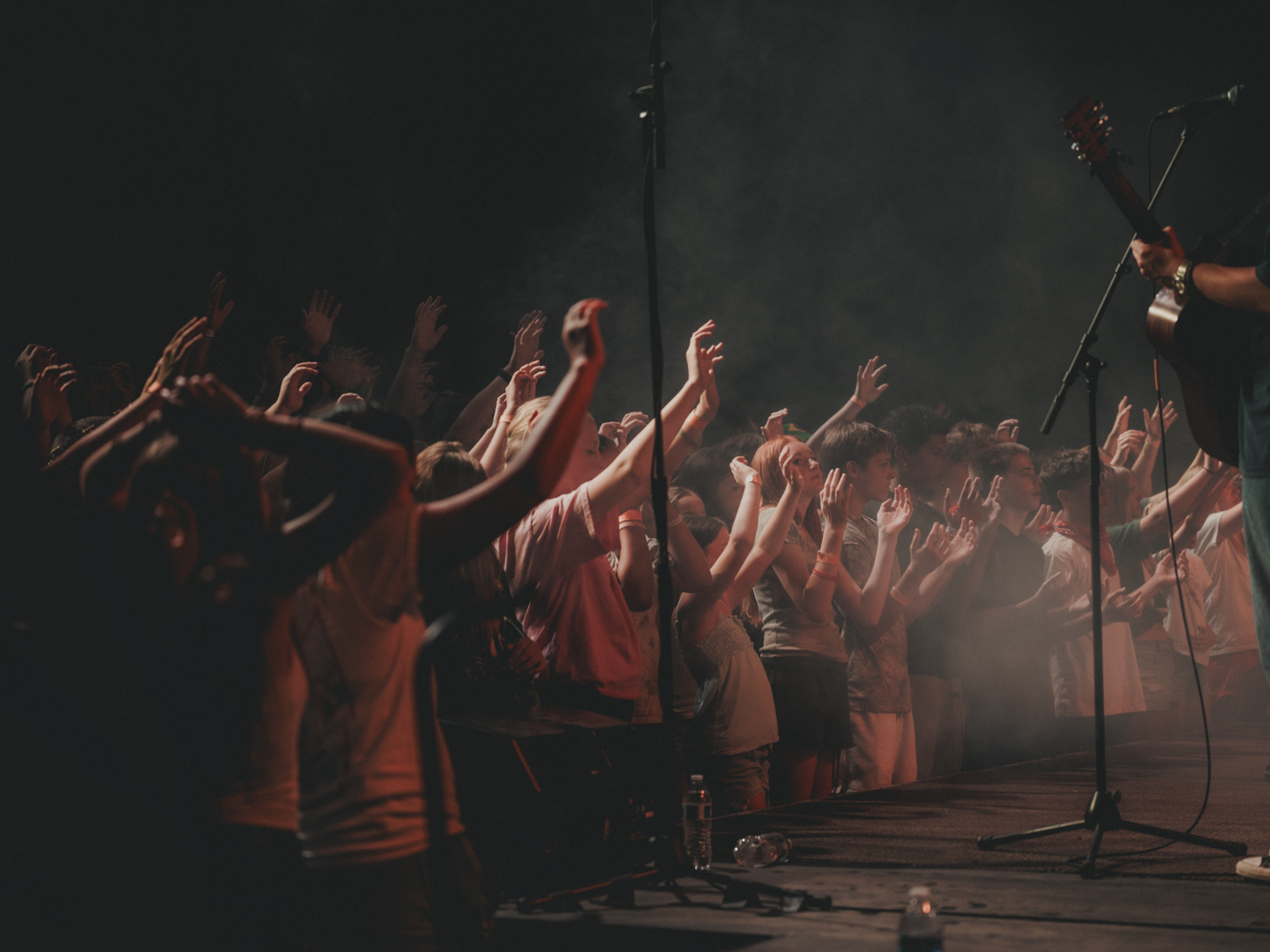 A crowd of students worshiping with hands raised toward the stage