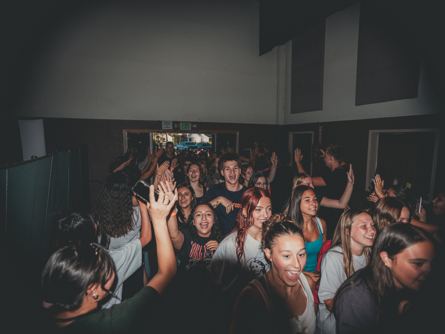 A packed room of students worshiping with hands raised